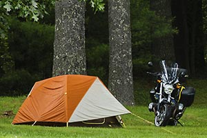 Motorcycle parked next to tent on the edge of the woods