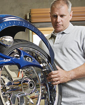 Man working on custom chrome rear wheel of metallic blue custom motorcycle