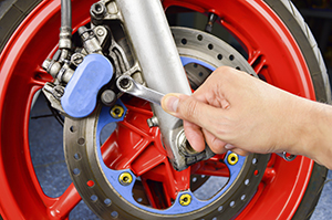 Man with cresent wrench working on red motorcycle wheel