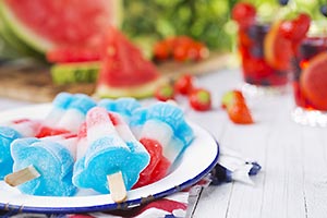 Red, White and Blue Popsicles on a plate with fruit in the background