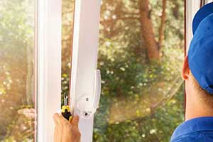 Man with blue ball cap and screw driver in hand putting a replacement window in place